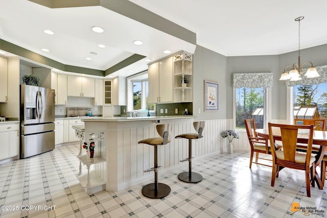 kitchen with stainless steel fridge, open shelves, plenty of natural light, a peninsula, and wainscoting
