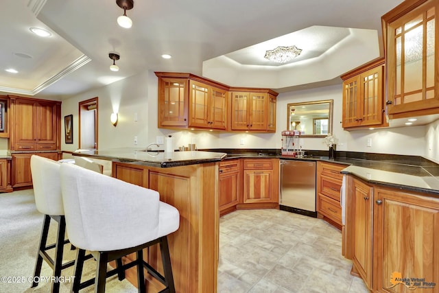 kitchen featuring a tray ceiling, brown cabinetry, a peninsula, a breakfast bar area, and glass insert cabinets