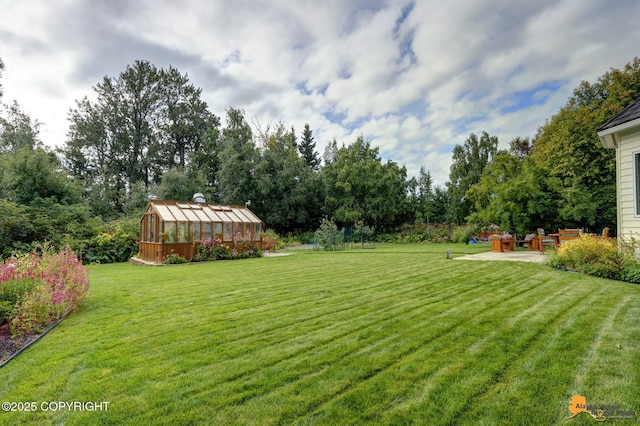 view of grassy yard with a greenhouse, an outdoor structure, and view of wooded area