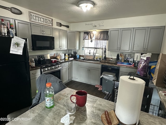 kitchen featuring black appliances, a sink, a textured ceiling, gray cabinetry, and dark wood finished floors