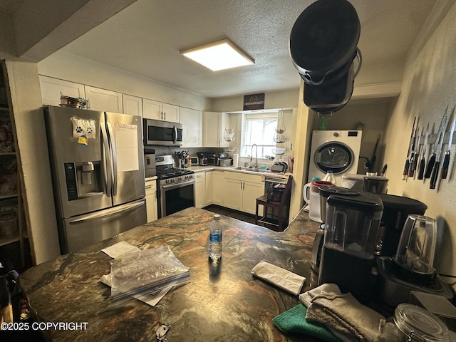 kitchen featuring appliances with stainless steel finishes, a sink, white cabinets, and washer / clothes dryer