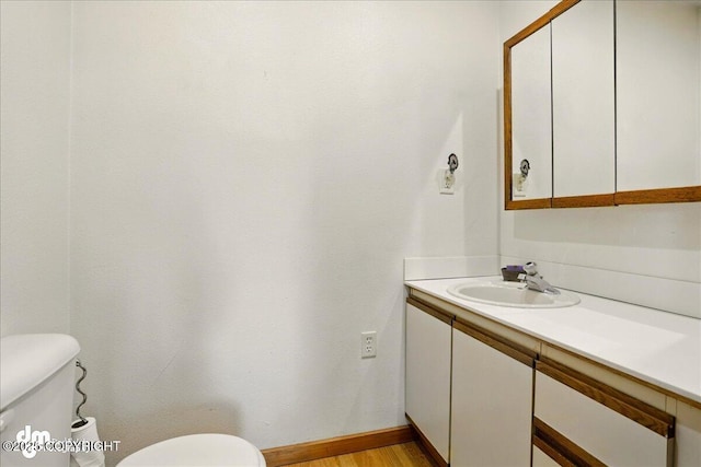 half bathroom featuring toilet, vanity, baseboards, and wood finished floors