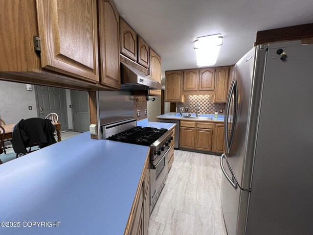 7700 Dover Ave, Anchorage, AK 99504 - kitchen featuring appliances with stainless steel finishes, under cabinet range hood, light countertops, backsplash, and brown cabinetry