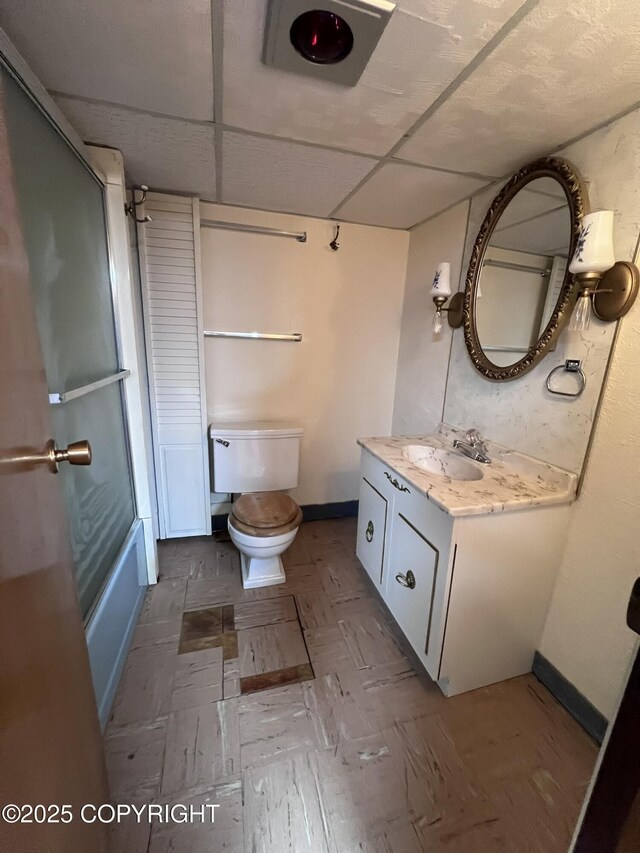 7700 Dover Ave, Anchorage, AK 99504 - bathroom with vanity, toilet, enclosed tub / shower combo, baseboards, and a paneled ceiling