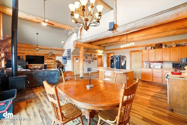dining space with rustic walls, a wood stove, light wood-style floors, beam ceiling, and high vaulted ceiling