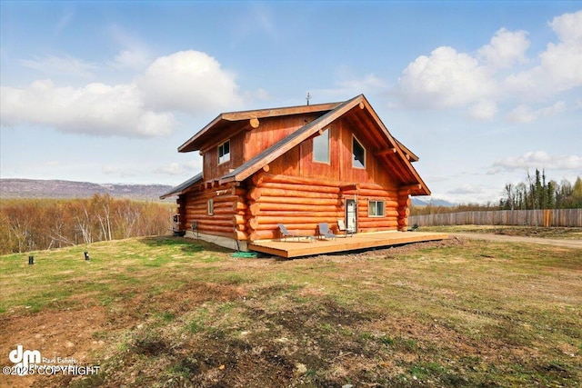 view of side of property with log exterior, a wooden deck, and a lawn