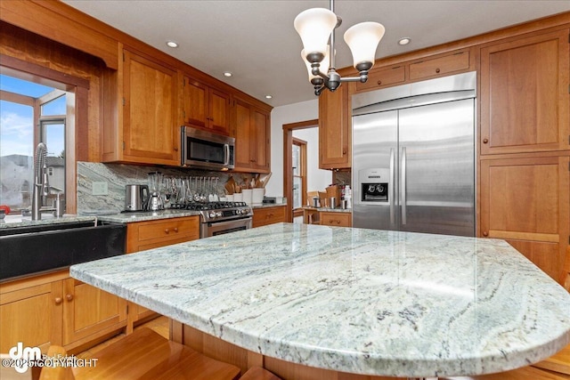 10613 Washington Cir, Anchorage, AK 99515 - kitchen featuring appliances with stainless steel finishes, a sink, brown cabinetry, light stone counters, and decorative backsplash