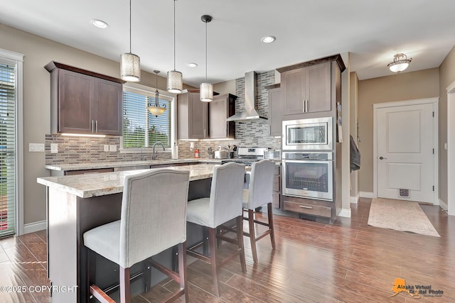 10588 E Nighthawk Cir, Palmer, AK 99645 - kitchen featuring stainless steel appliances, wall chimney range hood, baseboards, decorative backsplash, and a kitchen island