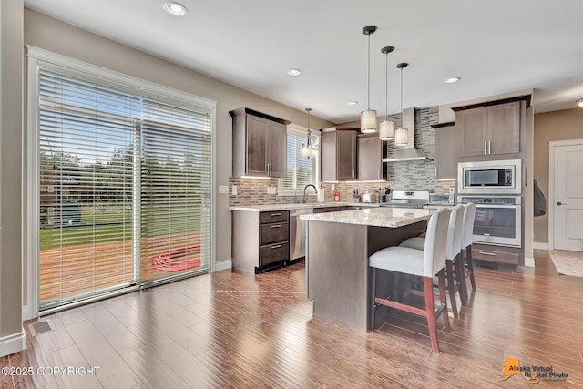 10588 E Nighthawk Cir, Palmer, AK 99645 - kitchen featuring wall chimney exhaust hood, stainless steel appliances, decorative backsplash, a breakfast bar, and a center island