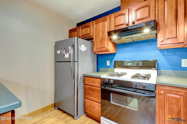 11721 Wranglers Way, Anchorage, AK 99516 - kitchen with gas range gas stove, under cabinet range hood, freestanding refrigerator, light wood-style flooring, and brown cabinetry