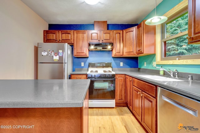 11721 Wranglers Way, Anchorage, AK 99516 - kitchen featuring appliances with stainless steel finishes, under cabinet range hood, brown cabinetry, light wood-type flooring, and hanging light fixtures