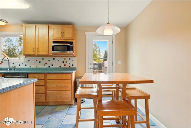 kitchen featuring appliances with stainless steel finishes, decorative backsplash, light brown cabinets, hanging light fixtures, and a sink