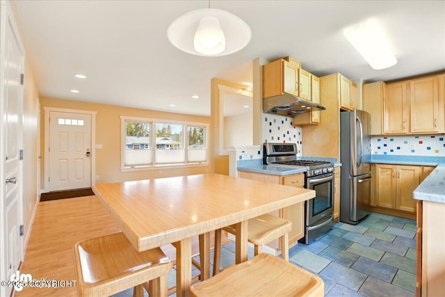 kitchen with stainless steel appliances, under cabinet range hood, backsplash, light brown cabinets, and light countertops