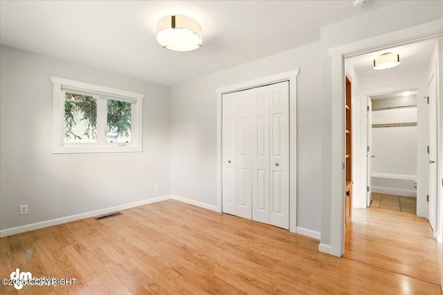 unfurnished bedroom featuring light wood-style flooring, a closet, and baseboards