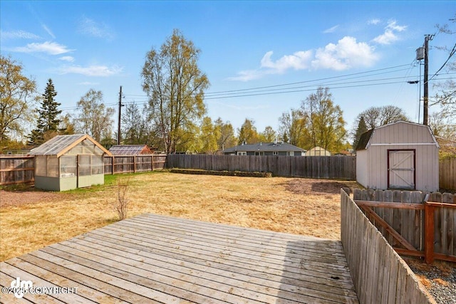 wooden deck featuring an outdoor structure, a greenhouse, and a shed