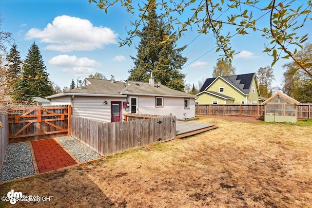 rear view of house with a greenhouse, an outbuilding, a deck, and a gate