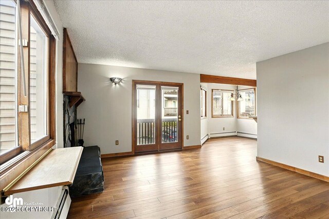 unfurnished living room with baseboard heating, a textured ceiling, wood finished floors, baseboards, and healthy amount of natural light