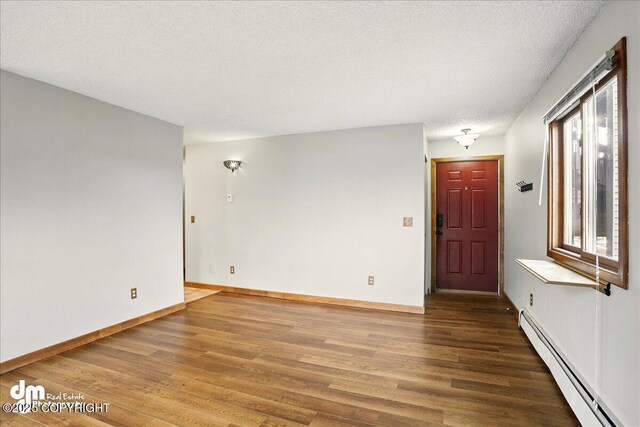 spare room featuring baseboard heating, wood finished floors, baseboards, and a textured ceiling