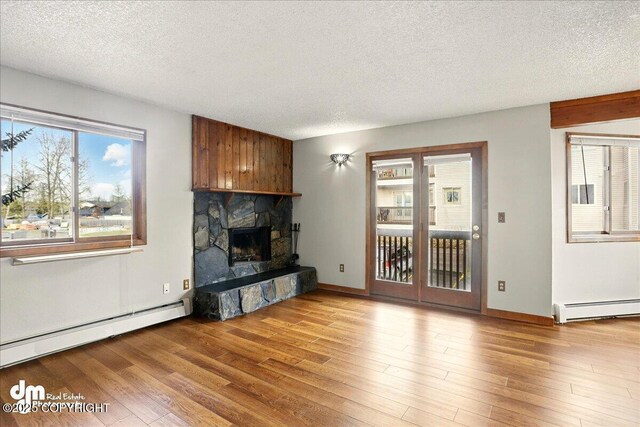 unfurnished living room featuring baseboard heating, a textured ceiling, a fireplace, and wood finished floors