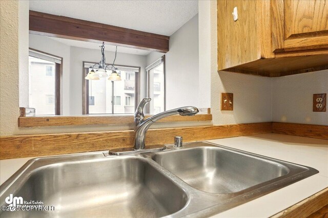 kitchen view of a sink, beamed ceiling, hanging light fixtures, light countertops, and a textured wall