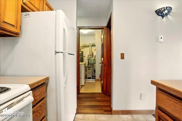 kitchen featuring freestanding refrigerator, brown cabinetry, baseboards, light countertops, and light tile patterned floors