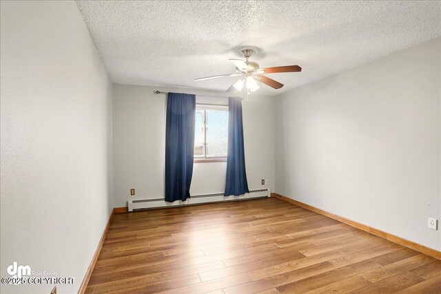empty room with a baseboard heating unit, light wood-type flooring, a ceiling fan, a textured ceiling, and baseboards
