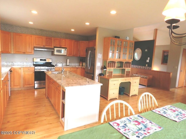 2340 E End Rd, Homer, AK 99603 - kitchen with stainless steel appliances, under cabinet range hood, light stone counters, light wood-type flooring, and an island with sink