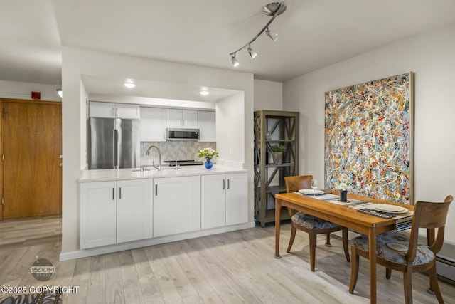 kitchen with stainless steel appliances, light countertops, light wood-type flooring, a sink, and backsplash