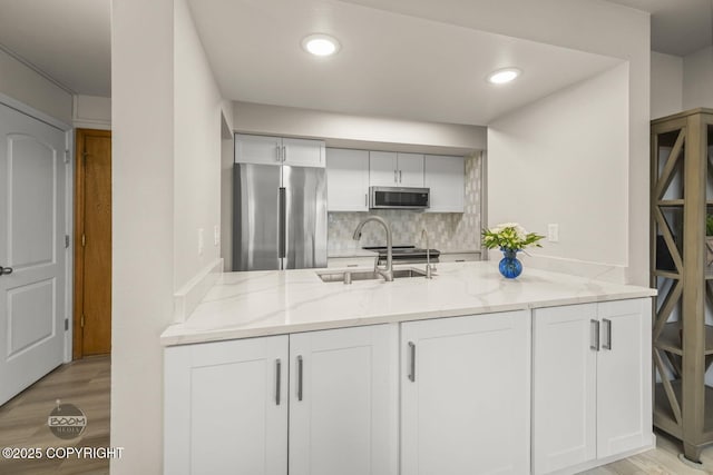 kitchen with appliances with stainless steel finishes, light stone counters, light wood-type flooring, white cabinetry, and decorative backsplash