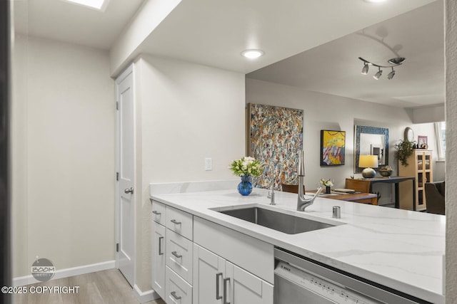 kitchen featuring dishwashing machine, a sink, light stone counters, light wood-type flooring, and white cabinetry