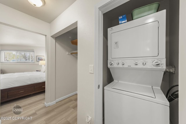 clothes washing area featuring stacked washer / drying machine, light wood-style flooring, and baseboards