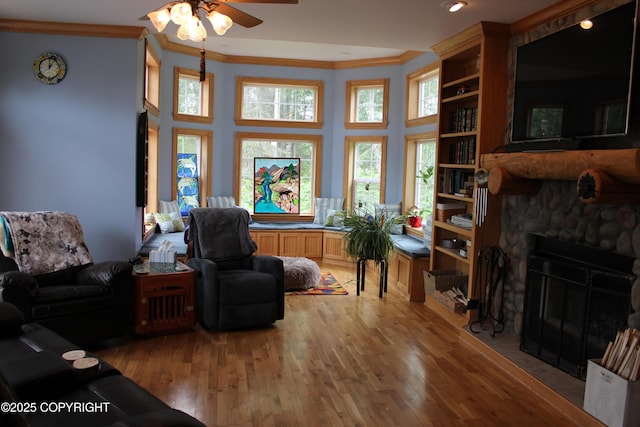 living area featuring ornamental molding, ceiling fan, light wood-style flooring, a fireplace, and a towering ceiling