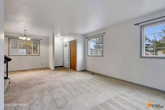 carpeted spare room featuring plenty of natural light, a chandelier, and baseboards
