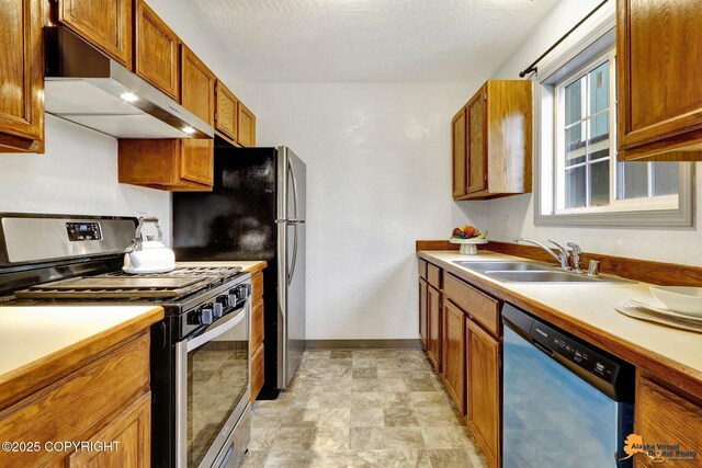 kitchen with gas stove, dishwasher, under cabinet range hood, a sink, and brown cabinets