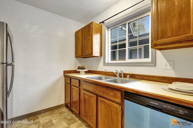 kitchen featuring stainless steel appliances, a sink, baseboards, brown cabinetry, and light countertops