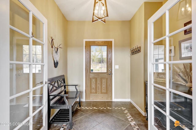 foyer with a chandelier, dark tile patterned floors, and baseboards