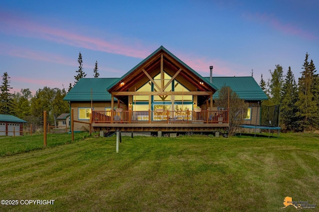 back of house at dusk featuring a lawn, a trampoline, and a deck