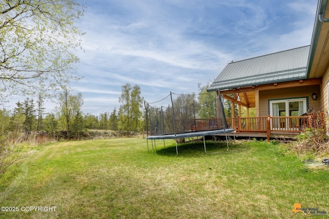 view of green lawn with a trampoline and a deck