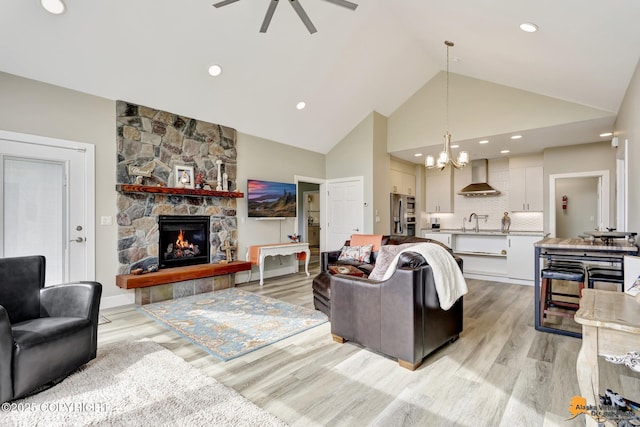 living room with high vaulted ceiling, a chandelier, a ceiling fan, a fireplace, and light wood-style floors