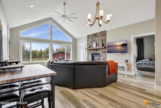 living area featuring a fireplace, light wood-type flooring, a chandelier, high vaulted ceiling, and ceiling fan