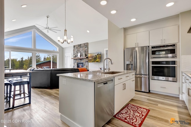 kitchen with stainless steel appliances, a sink, a fireplace, white cabinets, and a chandelier