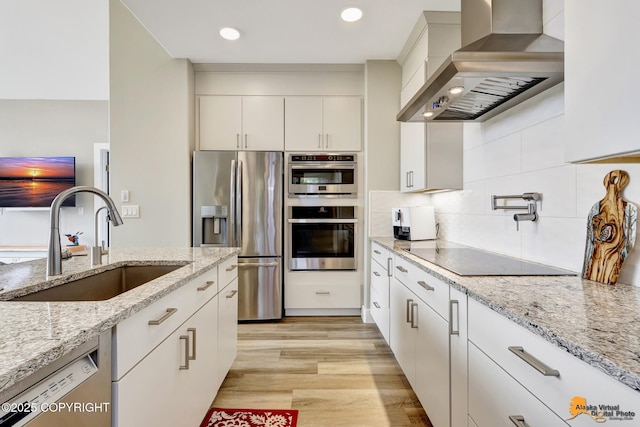 kitchen with stainless steel appliances, wall chimney exhaust hood, a sink, white cabinets, and light wood-type flooring