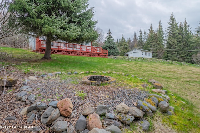 view of grassy yard featuring a fire pit, a wooden deck, and an outdoor structure