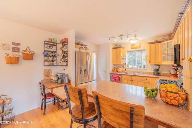 kitchen featuring appliances with stainless steel finishes, a sink, light brown cabinetry, light countertops, and a breakfast bar area