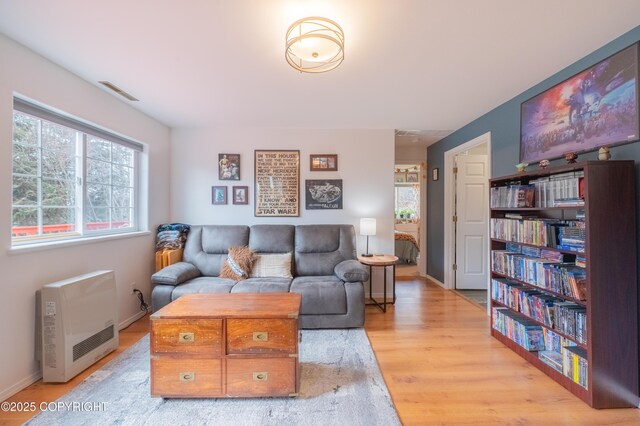 living area with light wood-type flooring, baseboards, and heating unit