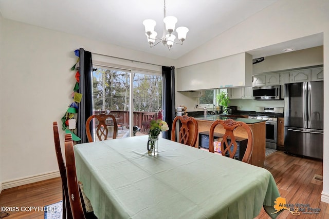dining space with a chandelier, wood finished floors, vaulted ceiling, and baseboards