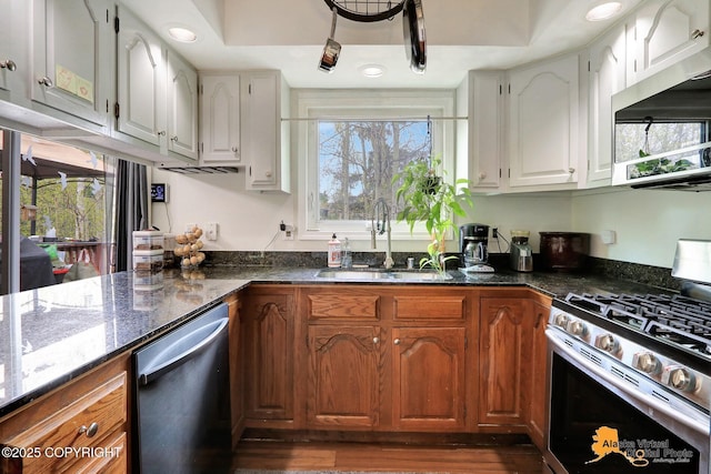 kitchen with appliances with stainless steel finishes, a sink, dark stone countertops, white cabinetry, and healthy amount of natural light