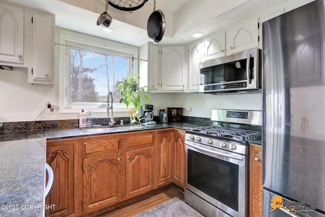 kitchen with stainless steel appliances, a sink, dark countertops, and white cabinetry