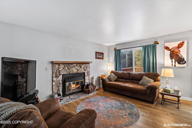 living room featuring a stone fireplace, wood finished floors, and baseboards