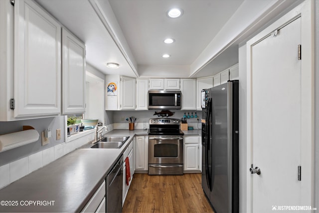 kitchen featuring appliances with stainless steel finishes, a sink, white cabinetry, dark wood-type flooring, and recessed lighting